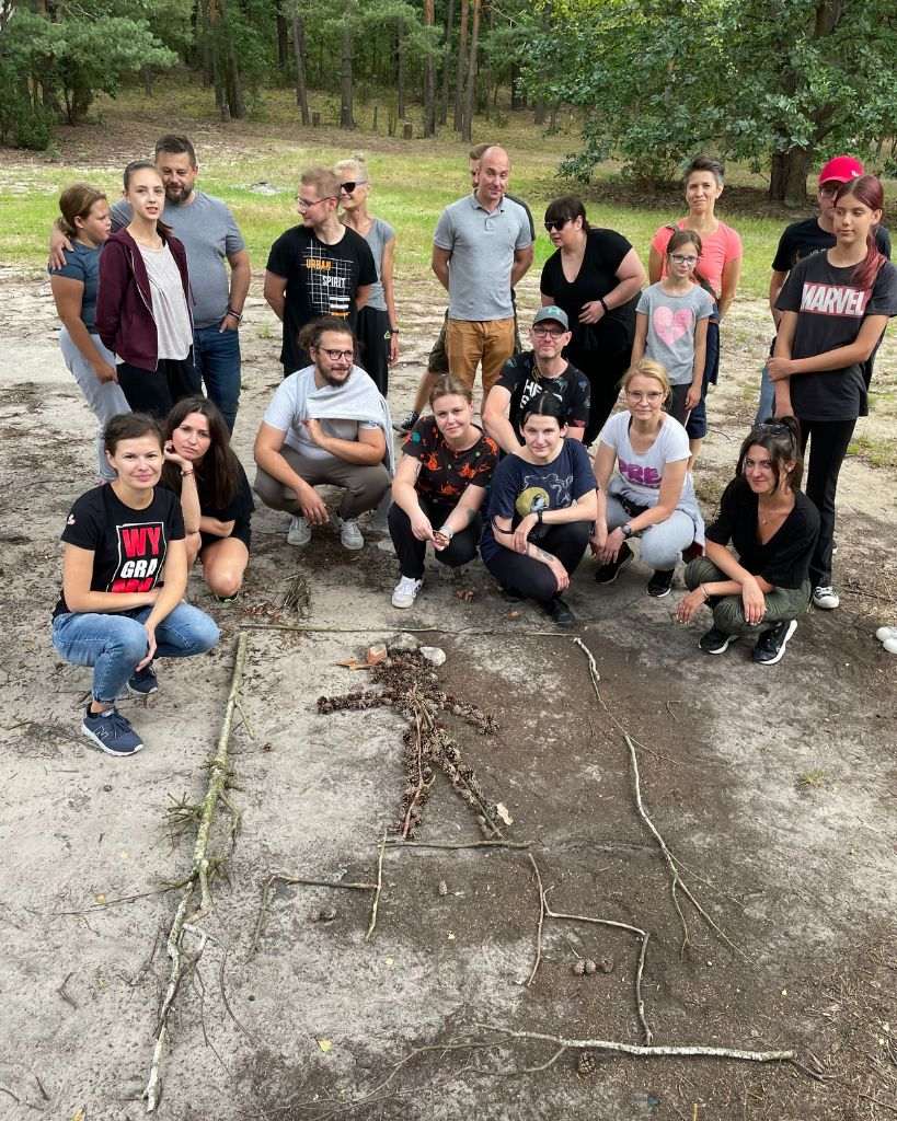 Uczestnicy integracji firmowej wykonują zadanie Land Art z wykorzystaniem szyszek na Polanie Pociecha w Kampinoskim Parku Narodowym.