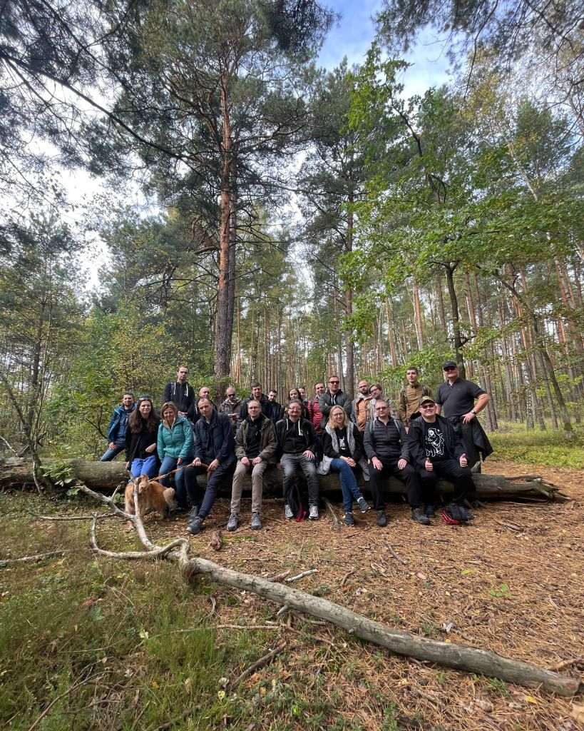Grupa uczestników wycieczki pozuje na powalonym drzewie podczas wycieczki w Kampinoskim Parku Narodowym.